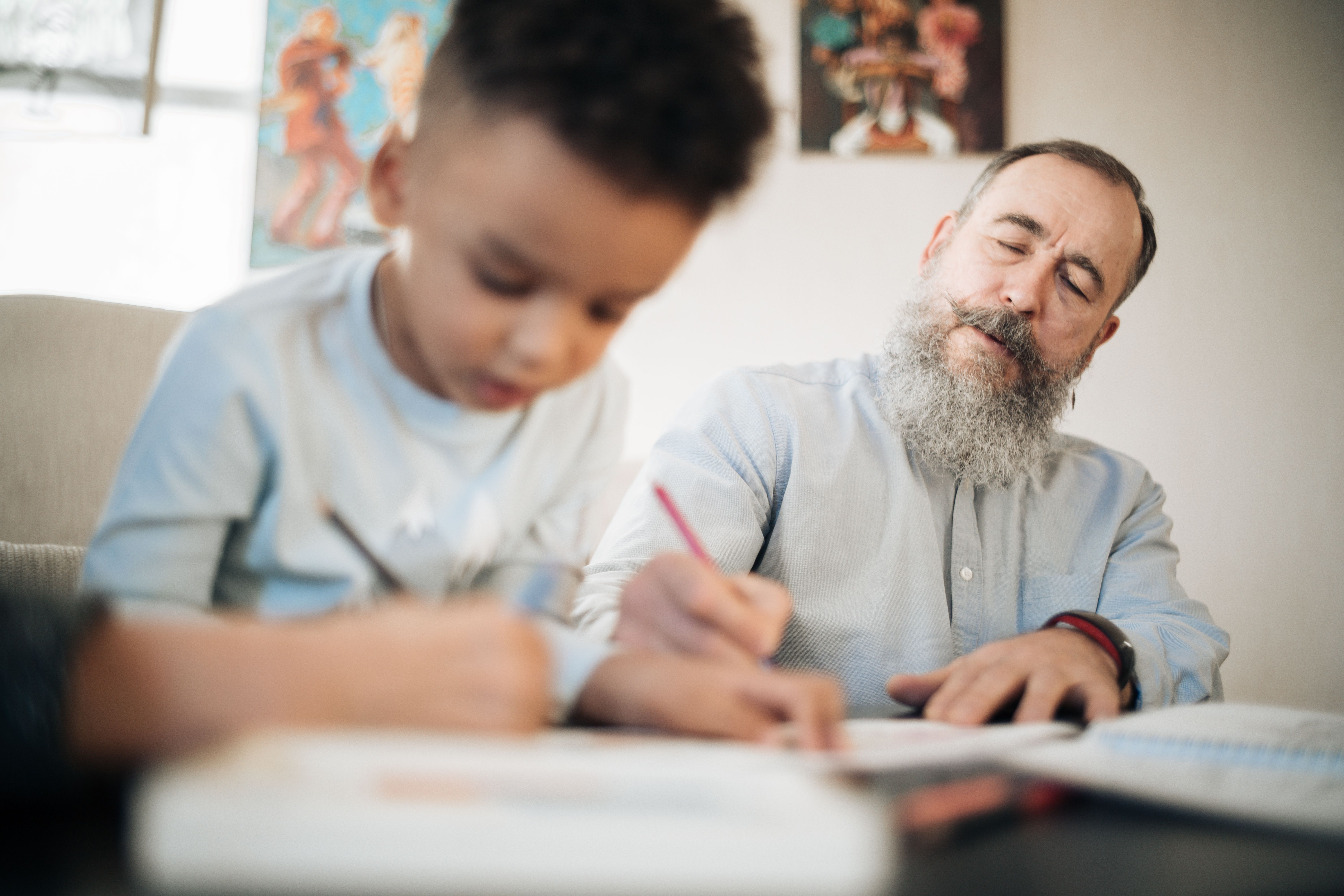Un uomo anziano affianca un bambino mentre scrive, in un momento di apprendimento condiviso.
